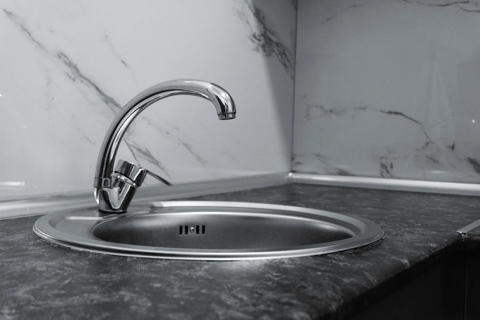 Stainless steel kitchen sink and faucet against marble backsplash in a modern kitchen.